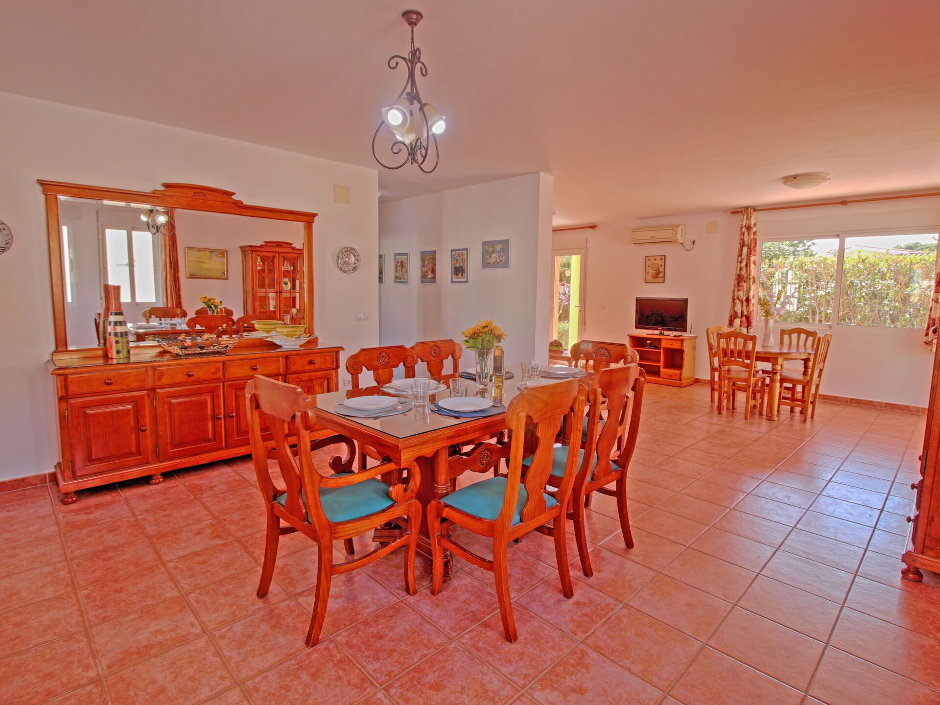 A spacious dining area with a wooden table and chairs, a large mirror, and a chandelier.