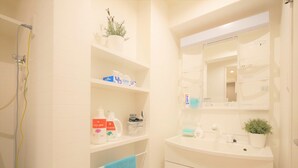 A bathroom with a white tiled wall, a shelf with toiletries, a mirror, and a sink with a potted plant.