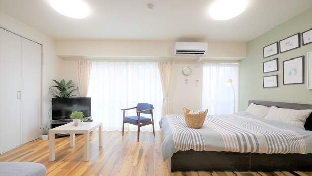 A room with a bed, a chair, a TV, a table, and a plant.