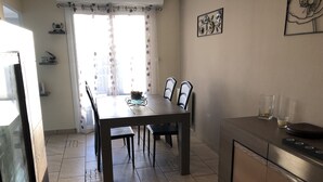 Un comedor con una mesa y sillas, una encimera de cocina y un ventanal con cortinas.