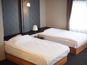 A hotel room with two single beds, a dark headboard, a bedside lamp, and a patterned wallpaper.