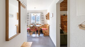 Ein schmales Entree mit einer hölzernen Bank, einem Esstisch mit Stühlen und Bergblick durch ein Fenster.