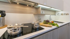 Une cuisine moderne dotée d’une plaque de cuisson à induction noire, de casseroles en acier inoxydable, d’une planche à découper en bois et de légumes frais.