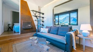 Un salon moderne avec un canapé, une table basse, un téléviseur et une grande fenêtre donnant sur les montagnes.
