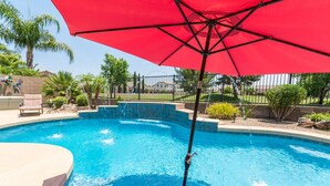 Ein Pool mit einem roten Sonnenschirm, umgeben von Palmen und einem Zaun.