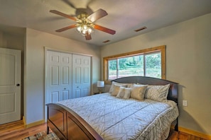 A bedroom with a bed, a ceiling fan, a window with a view of greenery, and a door. - Unique mountain home. 
Surround by trails, nature and a creek across the street
 (Cascade)