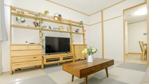A living room with a wooden TV stand, a flat-screen TV, a wooden coffee table, and a shelf with decorative items. - Nipponbashi Super House (Moriguchi)
