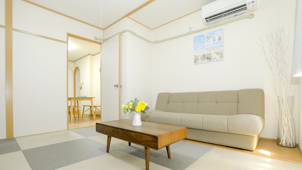 A living room with a sofa, a wooden coffee table with a vase of flowers, and a checkered floor. - Nipponbashi Super House (Moriguchi)