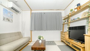 A living room with a sofa, a coffee table, a flat-screen TV, and a wooden TV stand with shelves. - Nipponbashi Super House (Moriguchi)