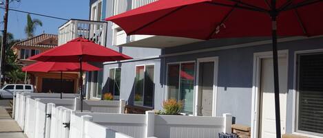 A coastal building with a balcony, red umbrellas, and a white picket fence.