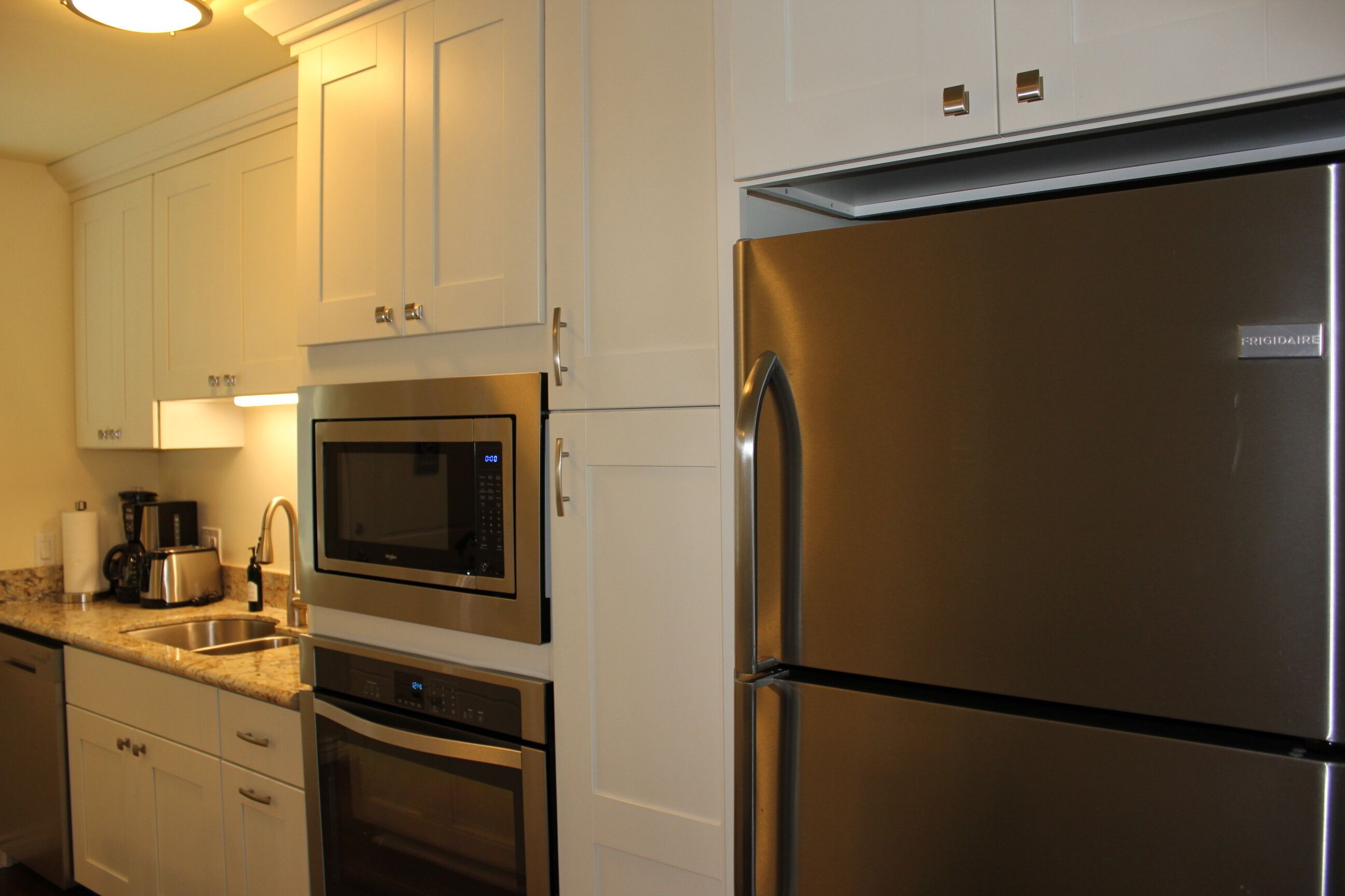 A kitchen with white cabinets, stainless steel appliances including a refrigerator, microwave, and dishwasher.