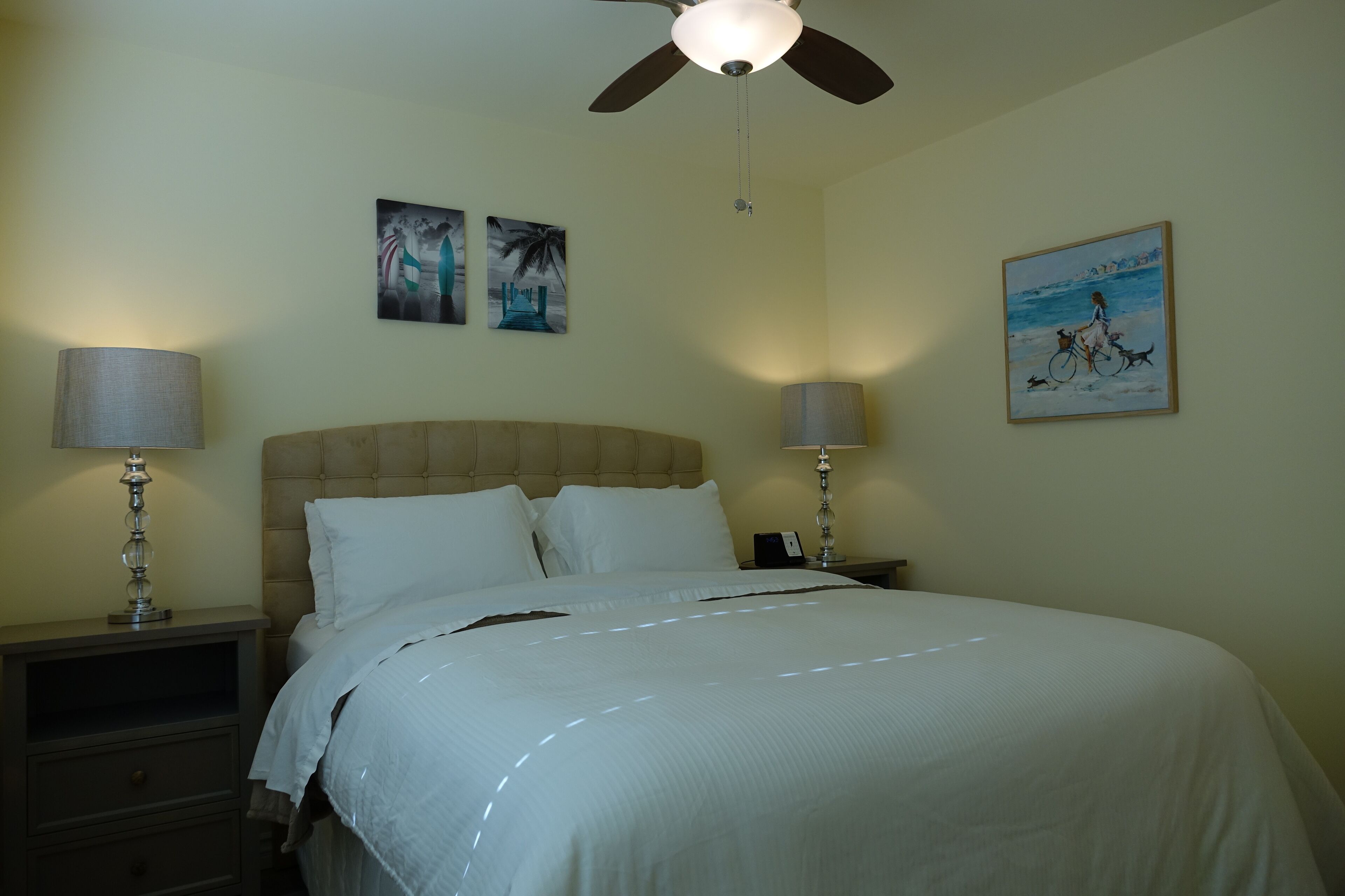 A bedroom with a bed, two bedside tables with lamps, a ceiling fan, and wall art.