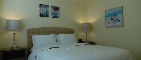 A bedroom with a bed, two bedside tables with lamps, a ceiling fan, and wall art.