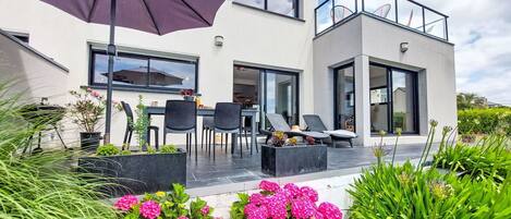 Ein modernes, zweistöckiges Haus mit einer Terrassenanlage, die Gartenmöbel und einen großen Sonnenschirm bietet.