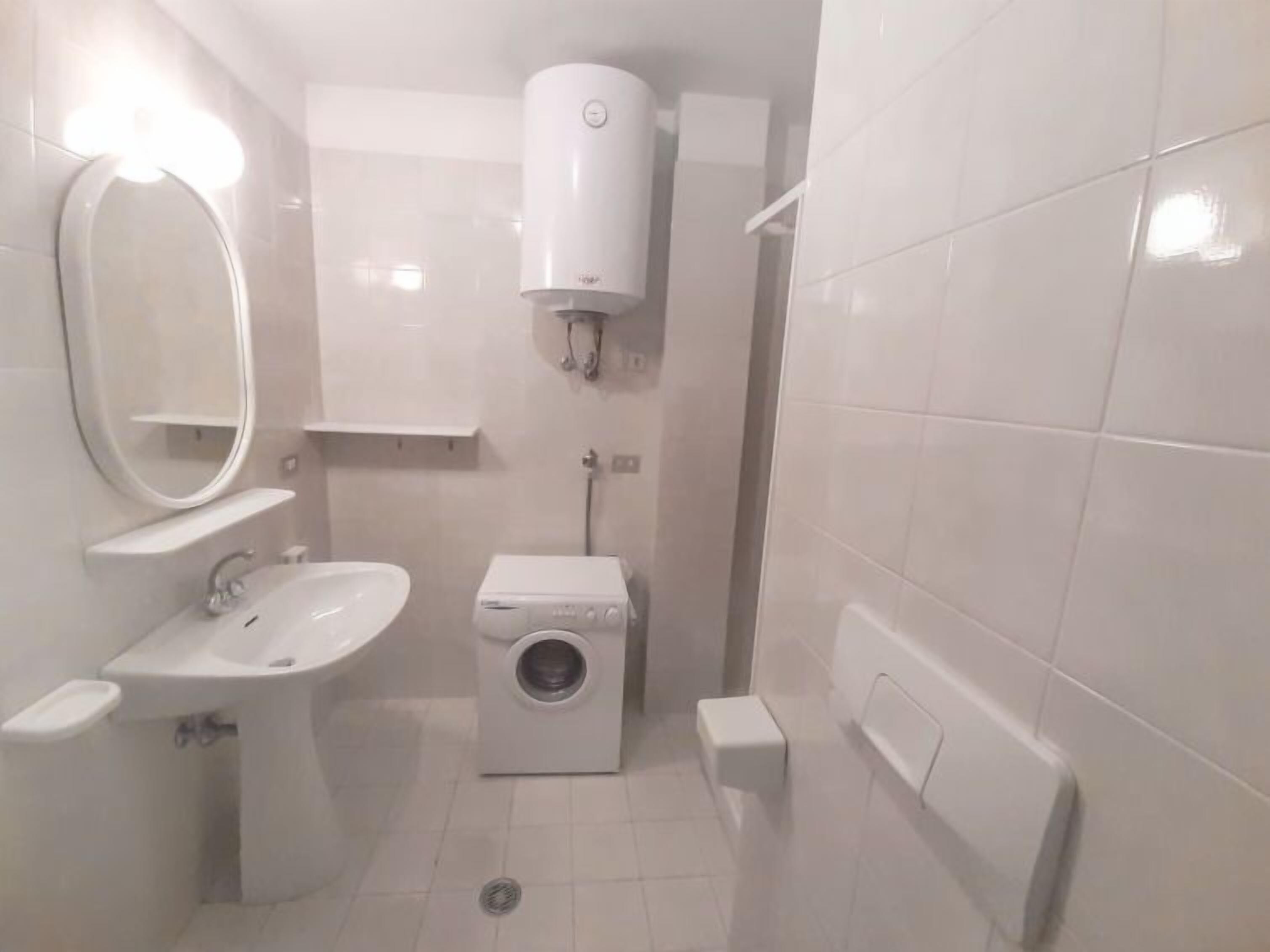 A compact bathroom with a sink, mirror, toilet, and a small washing machine.