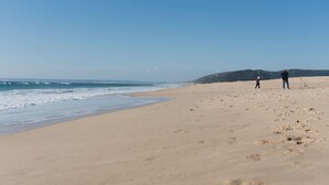 A wide sandy beach with ocean waves, a clear sky, and a hilly landscape in the distance. - Apartamento Cóncavos  (Zahara de los Atunes)