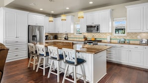 A modern kitchen with white cabinetry, a central island with bar stools, stainless steel appliances, and pendant lighting.