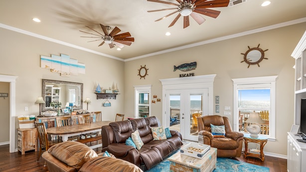 A spacious living room with a brown leather sofa, a dining area with a wooden table, and a view of the ocean through a large window.