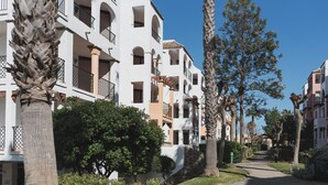 Un immeuble résidentiel doté de nombreux balcons, d’un chemin pavé et entouré de verdure.