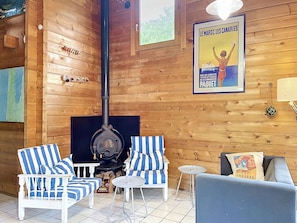 L'intérieur d'un chalet en bois, avec un poêle à bois, des chaises à rayures, un canapé et une affiche accrochée au mur.