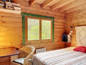 Une pièce de cabane en bois comprenant un lit, une chaise, une table et une fenêtre donnant sur la forêt.