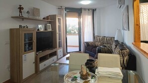 Un salon comprenant un téléviseur, un meuble en bois, un canapé et une table en verre agrémentée d ’un objet décoratif.