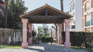 Un espacio al aire libre techado con techo de madera, pilares rosas y una entrada con portón.
