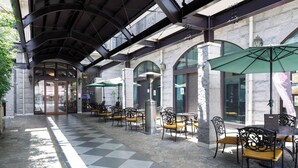 An outdoor cafe area with stone flooring, metal-framed tables and chairs, and green umbrellas providing shade. - FIVE HOTEL OSAKA (Osaka)