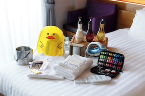 Una cama bien tendida con una variedad de artículos de aseo, incluyendo un patito de goma amarillo, un frasco de acondicionador y una paleta de maquillaje.