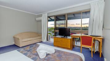 A hotel room with a bed, a sofa, a desk with a chair, a television, and a large window offering a view of the outdoors.