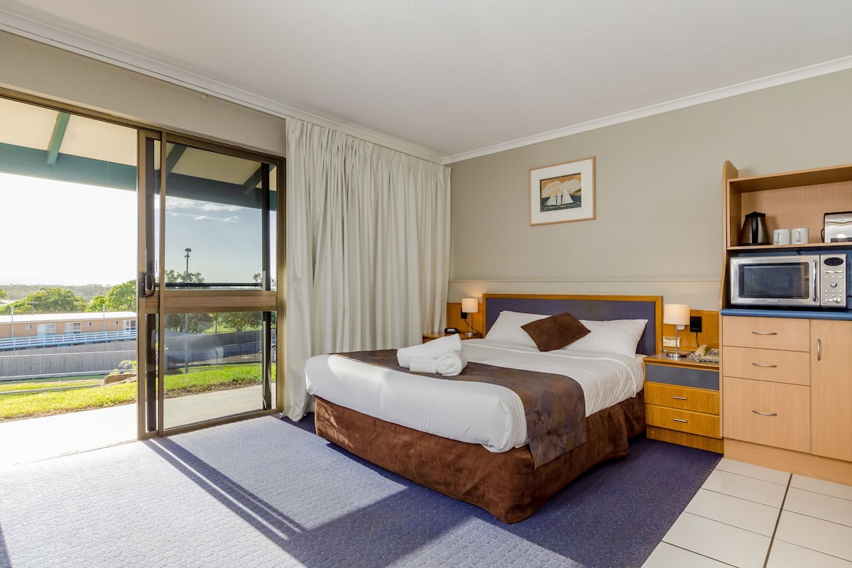 A hotel room with a large bed, a microwave, a nightstand, and a view of the outdoors.