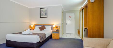 Habitación de hotel con cama, mesitas de noche, sofá, puerta y una lámpara fijada a la pared.