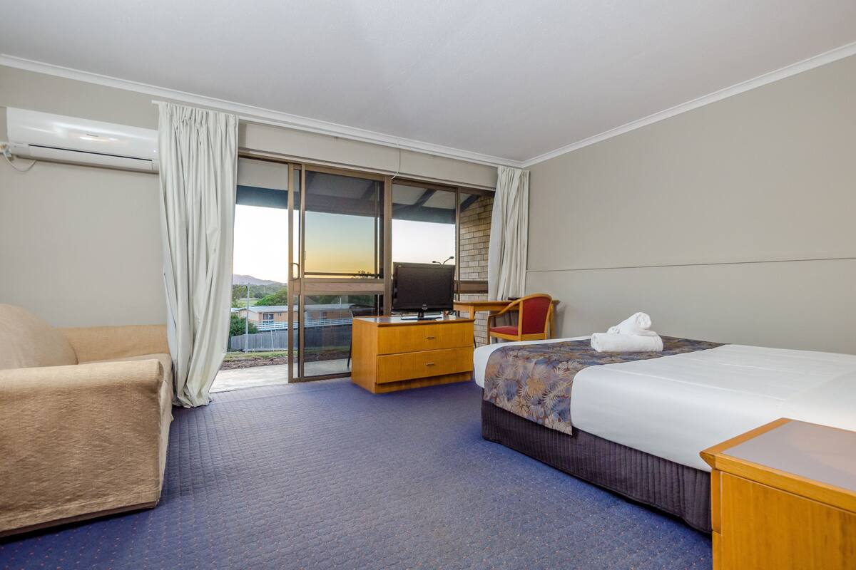 A hotel room with a bed, a TV, a desk, a chair, and a view of the outdoors.