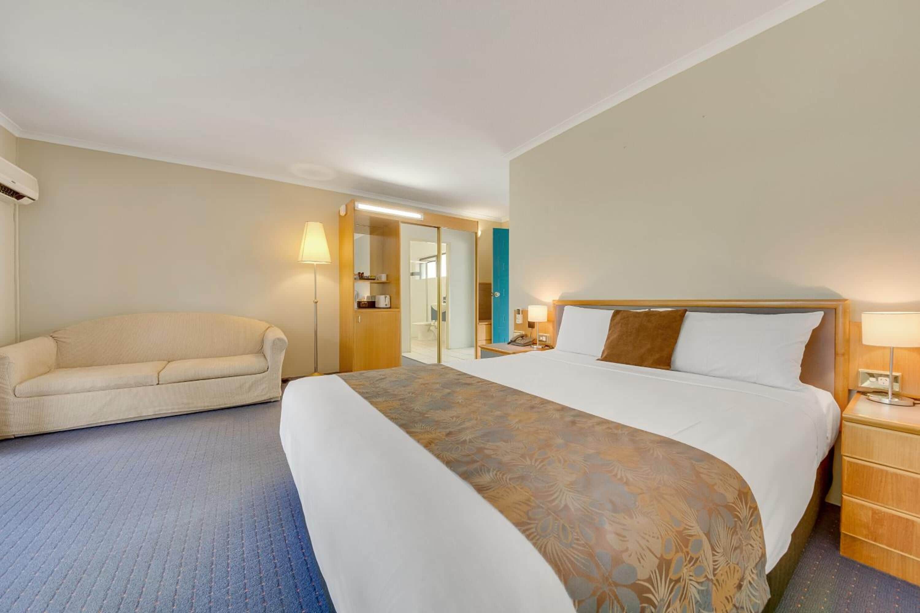 Ein Hotelzimmer mit einem großen Bett, einer Couch, einem Nachttisch mit Lampe und einem Kleiderschrank.