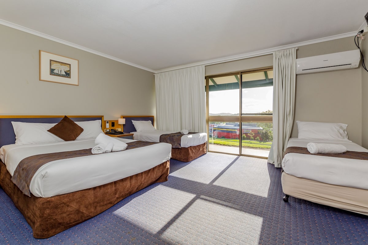 A hotel room with two beds, a large window with curtains, an air conditioning unit, and a framed picture on the wall.