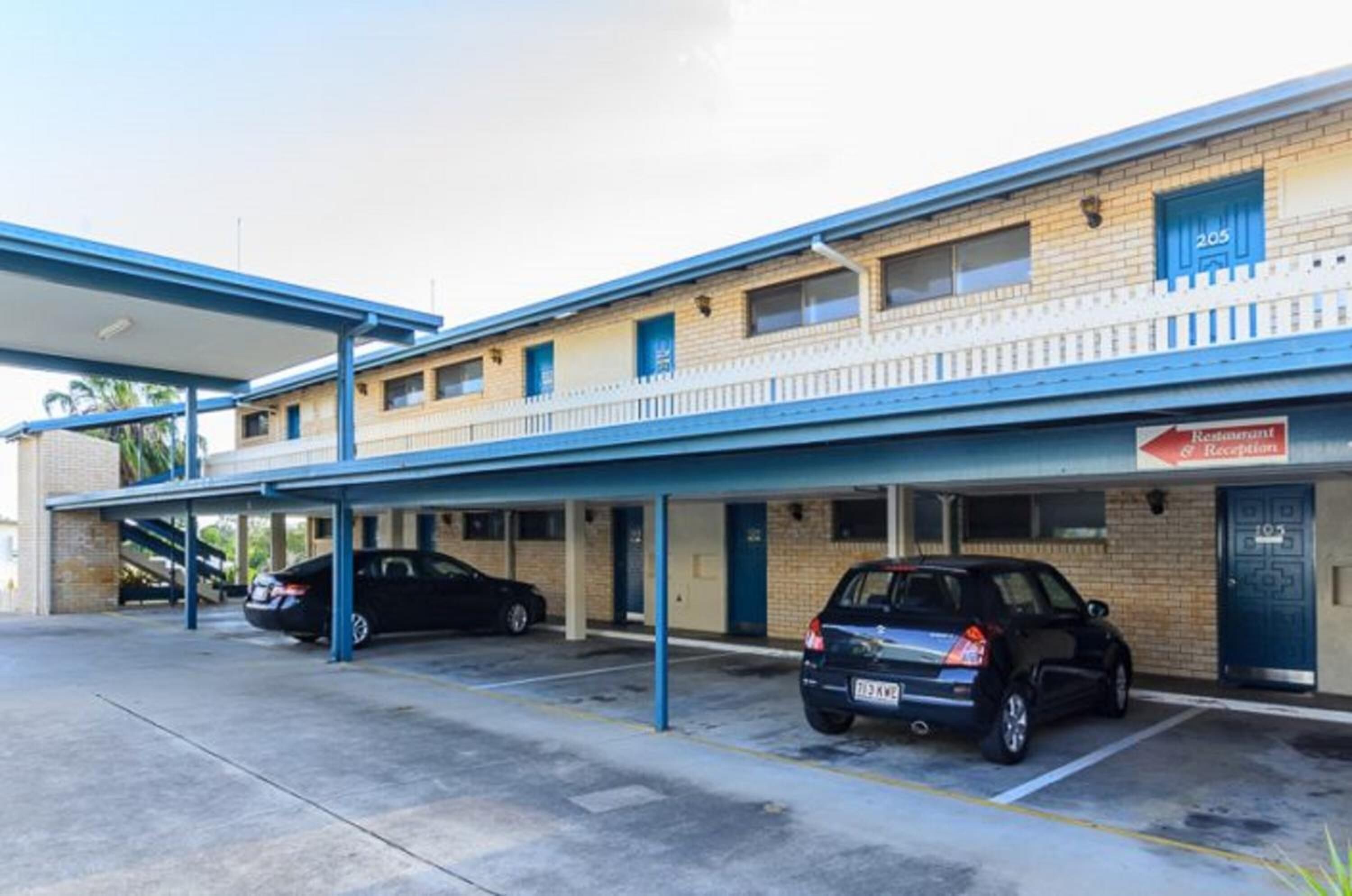 A motel with a covered parking area and two cars parked inside.