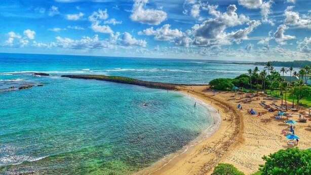 Una spiaggia con acque turchesi cristalline, una riva sabbiosa e alcuni ombrelloni.