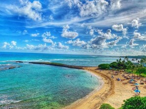 Uma praia com águas turquesa cristalinas, areal arenoso e alguns guarda-sóis.