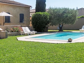 Une piscine avec des chaises longues, un arbre et un bâtiment doté d’un toit en tuiles.