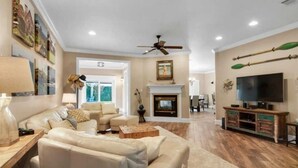A spacious living room with a fireplace, a television, and a ceiling fan. - 6 BR, Huge Pool/Jacuzzi, Movie Theater, Luxurious Yard, Discounted Golf Cart (Destin)
