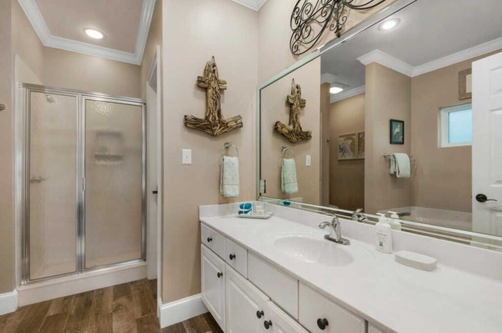 A bathroom with a shower, a large mirror, and a vanity with drawers and a sink.