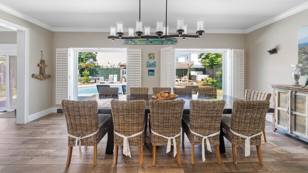 A dining area with a glass table surrounded by wicker chairs, a chandelier, and a view of a pool and outdoor seating. - 6 BR, Huge Pool/Jacuzzi, Movie Theater, Luxurious Yard, Discounted Golf Cart (Destin)