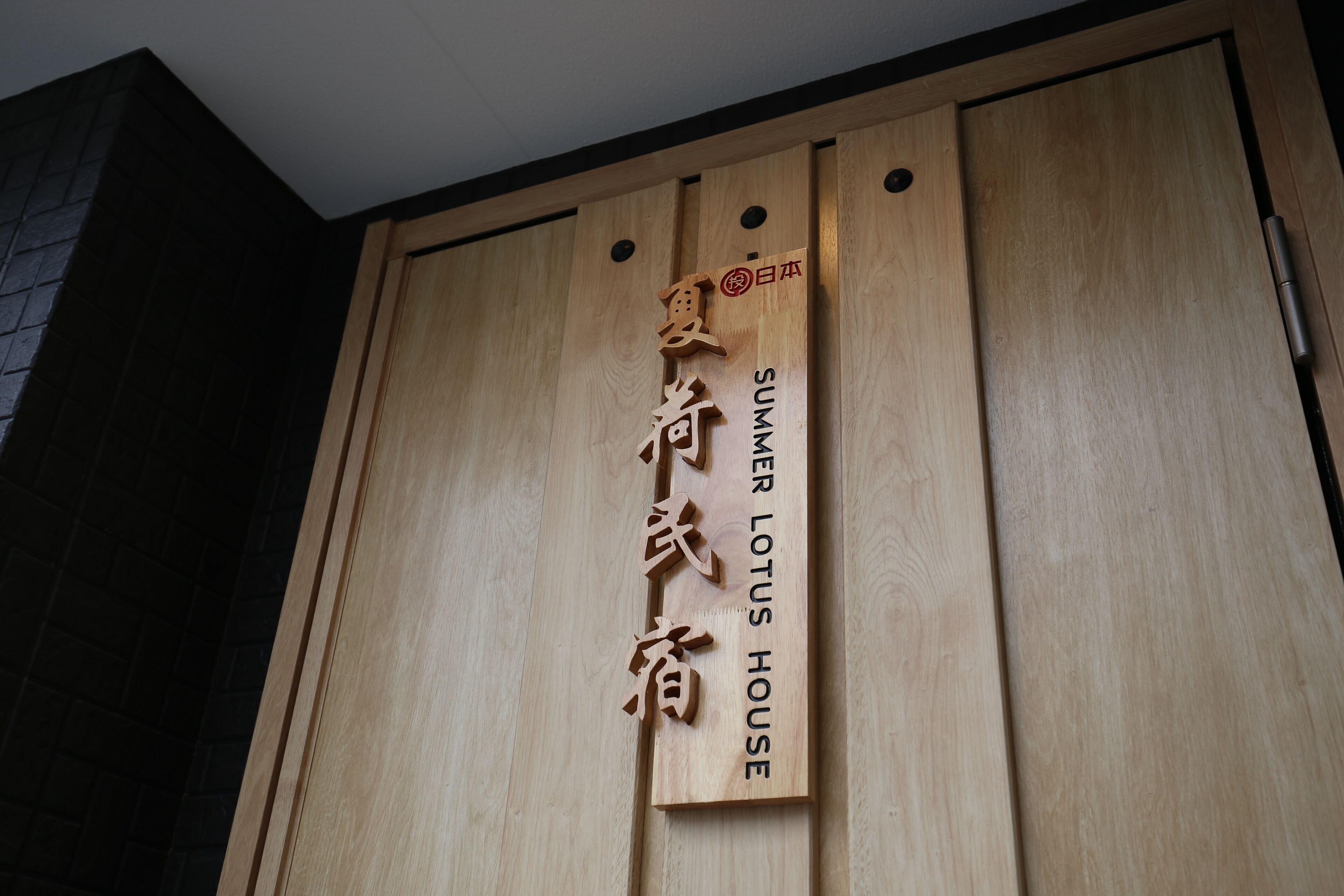 Une enseigne en bois ornée de caractères japonais et des mots anglais « SUMMER LOTUS HOUSE ».