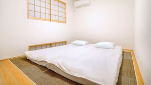 A single bed with white bedding, a wooden headboard, a shoji screen, and an air conditioning unit on the wall. - Summer Lotus House Osaka (Osaka)