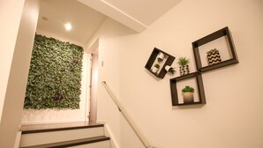 A staircase with a handrail, a wall with a green leafy wall panel, and three framed pictures with plants. - Summer Lotus House Osaka (Osaka)