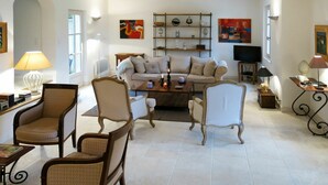 A spacious living room with a sofa set, armchairs, a coffee table, and a TV. There are shelves with decorative items and paintings on the walls. - Beautiful private villa for 8 guests with WIFI, private pool, TV, patio and pets allowed (Maussane-les-alpilles)