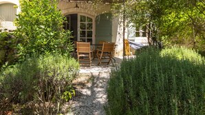 A covered outdoor seating area with wooden chairs and a table, surrounded by lush greenery and a gravel path. - Beautiful private villa for 8 guests with WIFI, private pool, TV, patio and pets allowed (Maussane-les-alpilles)