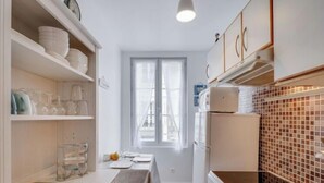 A compact kitchen with white cabinetry, a dining area with a table and chairs, and a window providing natural light. - Apartment Carnot by Interhome (Deauville-Trouville)