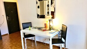 A dining area with a white table and two black chairs, a black door, and a wall-mounted mirror.