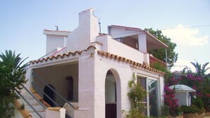 A two-story building with a white exterior, a covered porch, and a staircase leading to the entrance. - Studio apartment on rural smallholding, 3km from beaches and amenities (L'Ampolla)